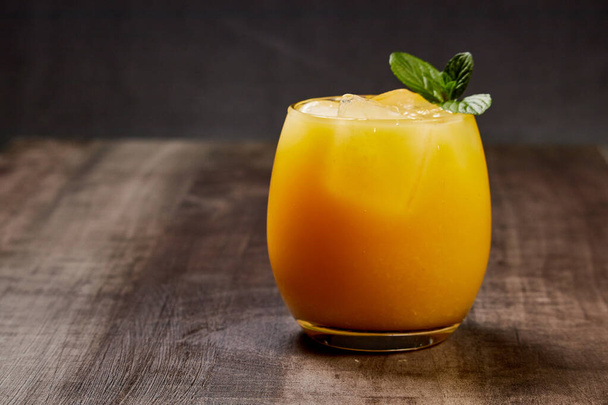 vaso refrescante con zumo de naranja, hielo y menta sobre una mesa de madera - Foto, Imagen