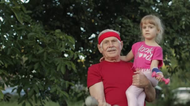 Wnuczka i dziadek ćwiczą fitness z hantlami. Starszy mężczyzna z dzieckiem dziewczynka - Materiał filmowy, wideo