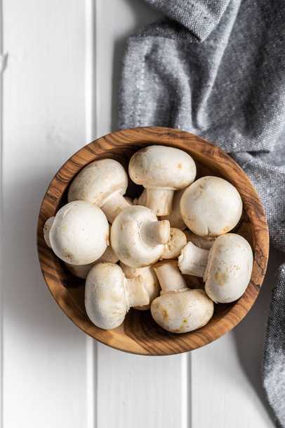 Fresh white champignon mushrooms in wooden bowl on white table. Top view. - Foto, imagen