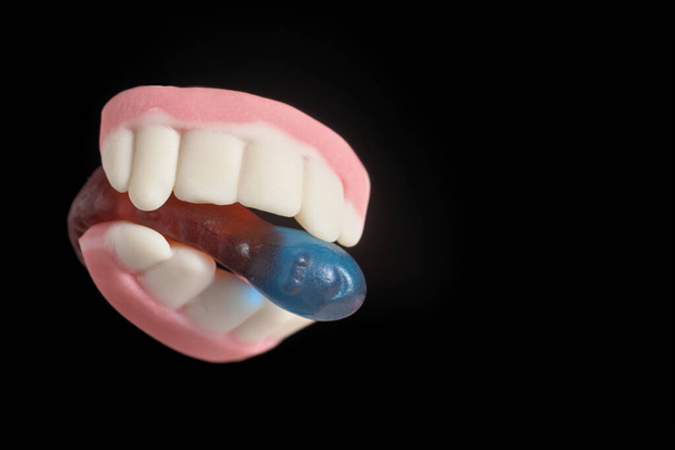 Halloween traktaties, kauwgom tanden bijten een gelei zoete worm, op zwarte achtergrond met kopieerruimte - Foto, afbeelding