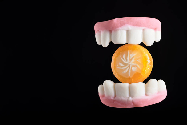 Gâteries d'Halloween, dents gommeuses mordant un bonbon orange, sur fond noir avec espace de copie - Photo, image