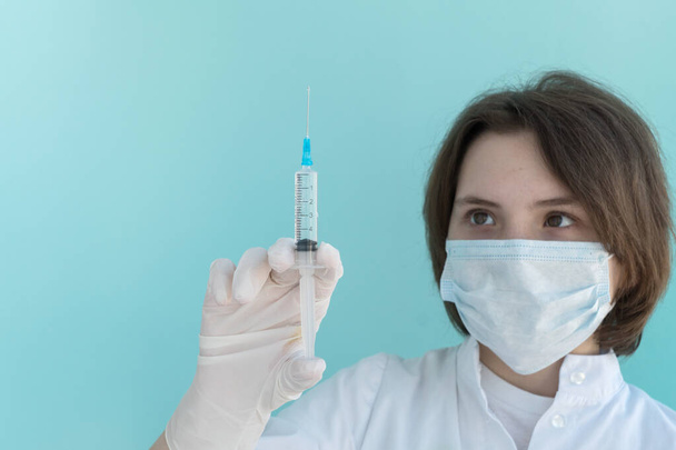 молода жінка-лікар в медичній масці тримає сироватку з рідкою медициною для вакцинації і дивиться на неї. Концепція охорони здоров'я. Захист від вірусів, грипу
. - Фото, зображення