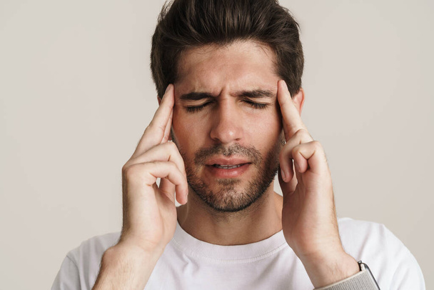 Image of unhappy young man with headache rubbing his temples isolated by white background - Photo, Image