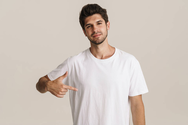 Image of confident young unshaven man pointing finger at himself isolated by beige background - Fotografie, Obrázek