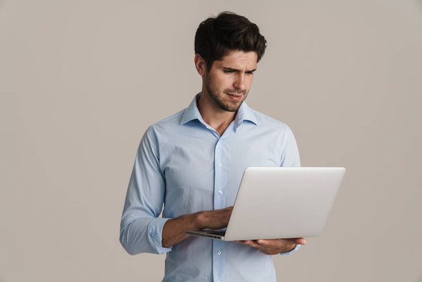 Image of serious businesslike brunette man working with laptop isolated by beige background - Photo, Image