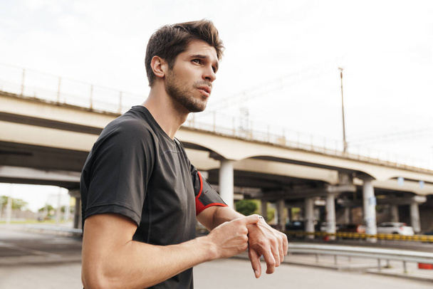Image of athletic young sportsman using smartwatch while working out on city street - Foto, imagen
