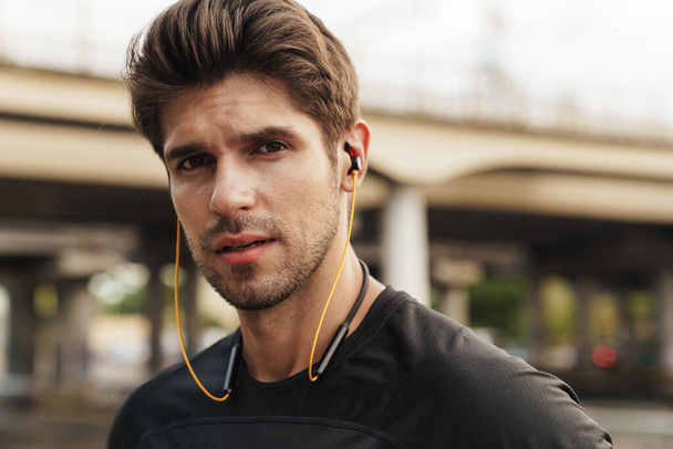 Image of athletic caucasian sportsman using earphones while working out on city street - Fotó, kép