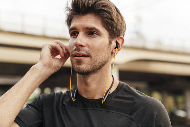 Image of athletic caucasian sportsman using earphones while working out on city street - Foto, Imagen