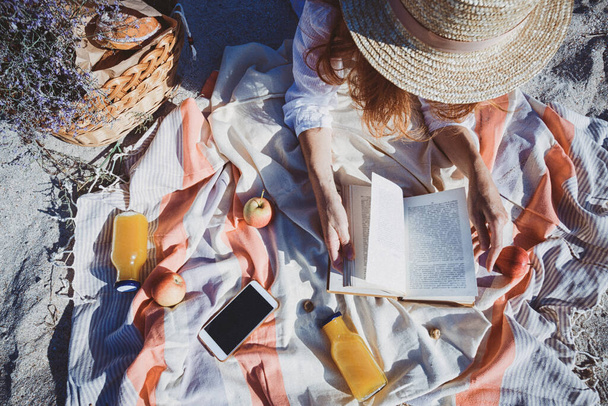 Léto - piknik u moře. košík na piknik s houskami, jablky a džusem. dívka na piknik lže a čte boo - Fotografie, Obrázek