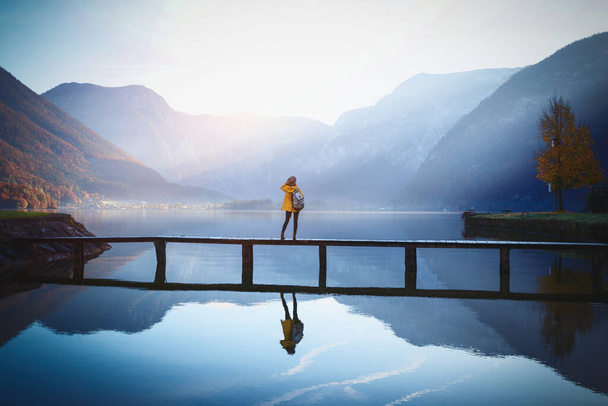 Mädchen steht am frühen Morgen auf einer Holzbrücke an einem Bergsee. schöne Landschaft und reflectio - Foto, Bild