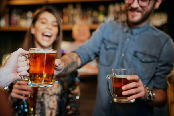 Close-up van de man die bier doorgeven aan zijn vriend terwijl hij in een pub staat. - Foto, afbeelding