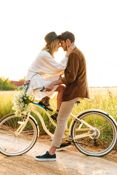 Image of young caucasian couple kissing while riding bicycle together in countryside - Foto, immagini