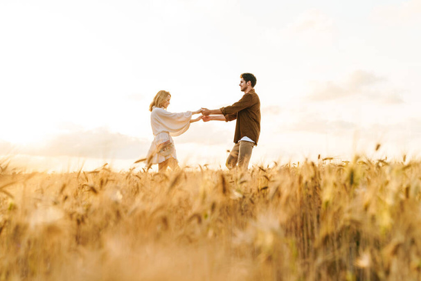Image of young caucasian beautiful couple dancing together in golden field on countryside - Photo, Image