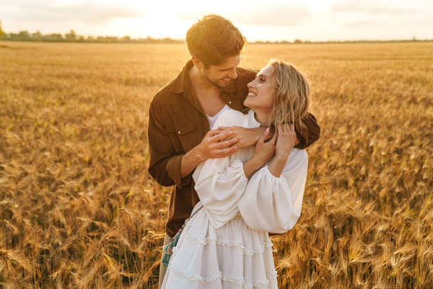 Image of young caucasian beautiful couple hugging together in golden field on countryside - Foto, Imagem