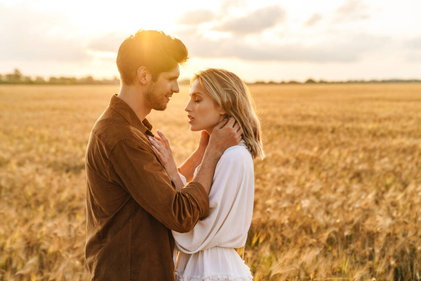 Image of young caucasian beautiful couple hugging together in golden field on countryside - Foto, Bild