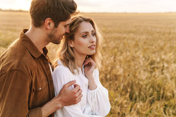 Image of young caucasian beautiful couple hugging together in golden field on countryside - Foto, afbeelding