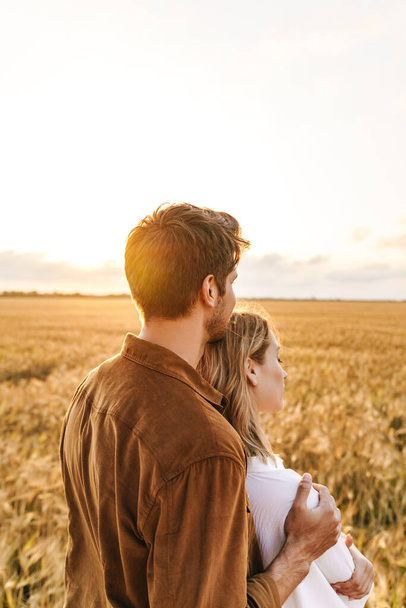Image of young caucasian beautiful couple hugging together in golden field on countryside - 写真・画像