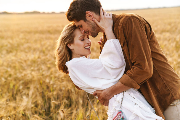 Image of young caucasian beautiful couple hugging together in golden field on countryside - Zdjęcie, obraz