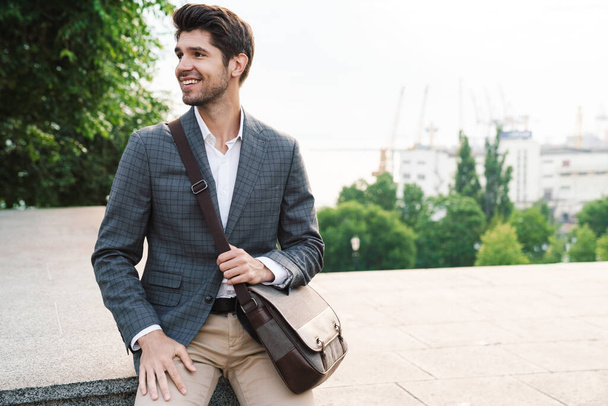 Image of a pleased smiling handsome business man outdoors with bag - Фото, зображення