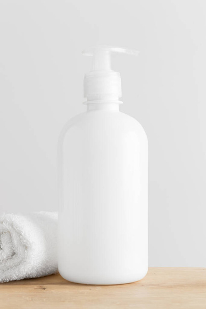 Maqueta de botella de dispensador de jabón líquido cosmético blanco con una toalla en una mesa de madera. - Foto, Imagen