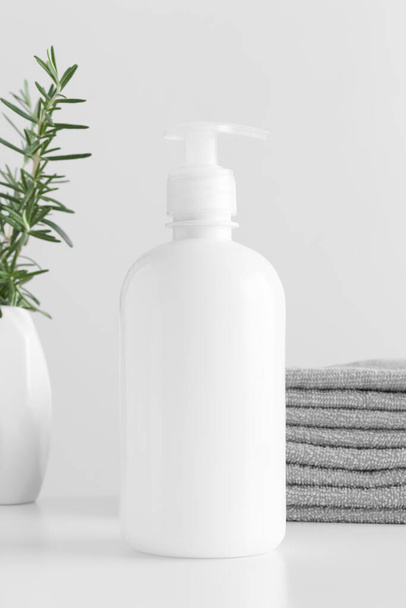 Botella dispensadora de jabón líquido cosmético blanco maqueta con toallas y un romero en una mesa blanca. - Foto, Imagen