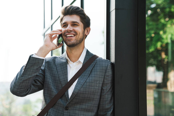 Image of a smiling cheery handsome business man outdoors talking by mobile phone - Photo, Image