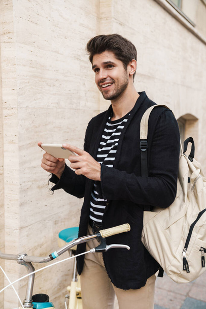 Image of a young positive smiling business man outdoors using mobile phone on a bicycle - Fotografie, Obrázek