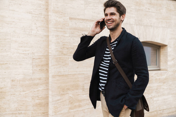 Image of a cheerful young business man outdoors talking by mobile phone - Fotoğraf, Görsel