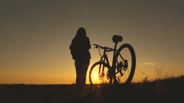 Kostenlose Mädchen reist mit einem Fahrrad bei Sonnenuntergang. Konzept von Abenteuer und Reisen. einsame Radfahrerin rastet im Park aus. Wanderin gesunde junge Frau steht auf Hügel neben Fahrrad und genießt Natur und Sonne. - Filmmaterial, Video