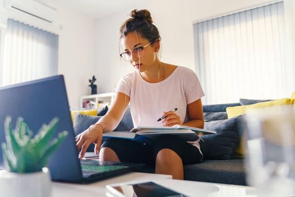 Widok z przodu na młodych kobiet kaukaskie badania przed laptopem komputera w domu - Dziewczyna czytanie książki przygotowującej egzamin po konsultacji online - edukacja i nauka koncepcja - Zdjęcie, obraz