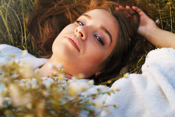 Close up portrait of young beautiful woman bride pretty girl lying on the field in summer day holding flowers looking to the camera - Natural beauty loneliness and love concept - Foto, imagen