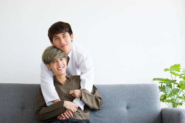 Feliz asiática masculina homosexual o parejas gay están sentados en el sofá cama, Ambos se abrazan con amor y calidez y mirando a la cámara. Concepto de orgullo LGBTQ. - Foto, imagen