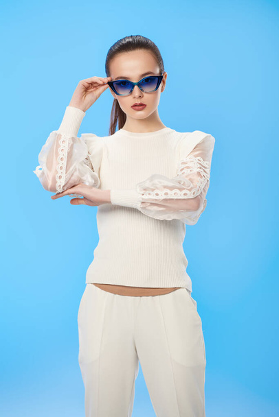 Beautiful summer girl posing in elegant white clothes and sunglasses on a light blue background. Happy smiling girl. Summer fashion and makeup. - Foto, afbeelding