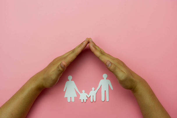 Вид зверху Руки захищає ланцюговий сімейний папір на рожевому тлі. Концепція страхування сім'ї, любові та благодійності
 . - Фото, зображення