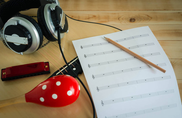Koncepcja instrumentów muzycznych. Zamknij się muzyk pisząc notatkę na papierze do tworzenia piosenki z grupą narzędzi muzycznych gitara, słuchawki, marakasy i harmonijki w godzinach porannych. - Zdjęcie, obraz