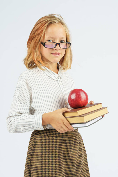 Ragazza adolescente in bicchieri che tiene una mela e un libro nelle sue mani. Sfondo isolato. Concetto educativo. - Foto, immagini