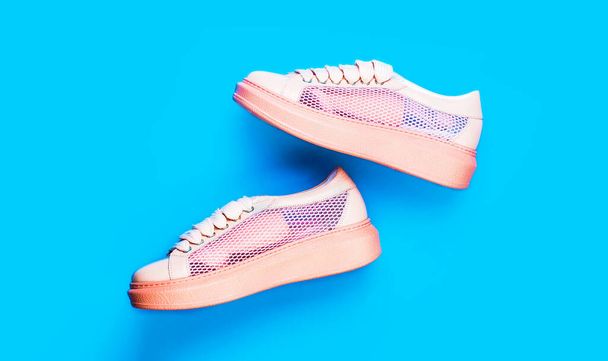 Overhead shot of running shoes. Close up, modern man sports shoe. Sneakers isolated on blue background, fashion. Sport shoes. Pair of pink sport shoes on blue background - 写真・画像