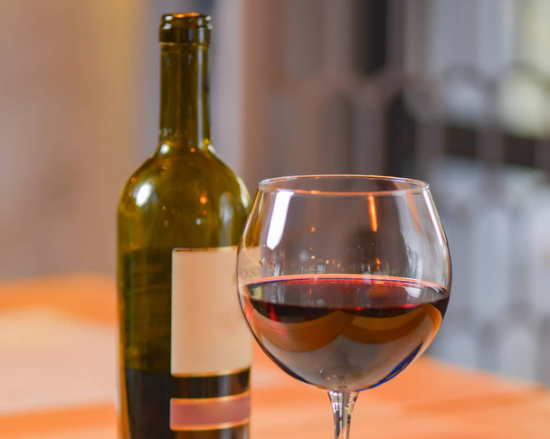 Wine glass and bottle of red wine on a wooden table over blurred background. Restaurant service, eating out concept. Drinking alcohol in a restaurant, celebration. - Photo, image