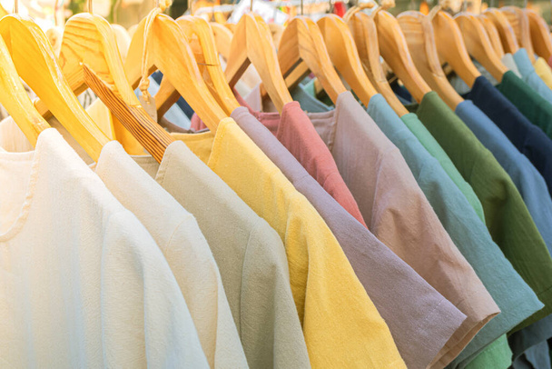 Bright colored clothes on wooden hangers on the market, Clothes shop in the outdoor market, Clothing trade. - Photo, Image