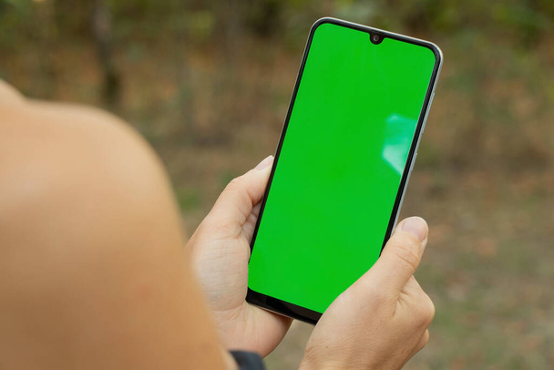 manos femeninas sosteniendo el teléfono con pantalla verde en el parque de verano de cerca - Foto, Imagen