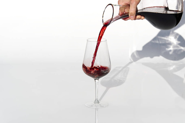 ソムリエは白を背景にデカンターからワイングラスに赤ワインを注ぐ. - 写真・画像