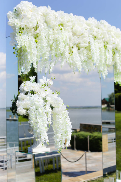白いアカシアで飾られた素晴らしい結婚式のアーチ、バックグラウンドで湖. - 写真・画像