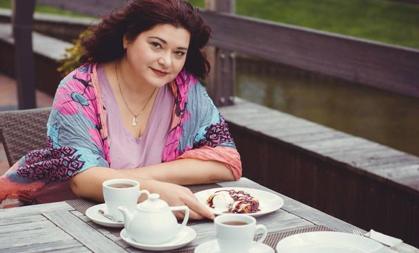 Mature woman, size plus american or European appearance sitting in a restaurant drinks coffee at autumn day. Lady with excess weight, stylishly dressed in cafe waiting for a friend - Foto, Bild