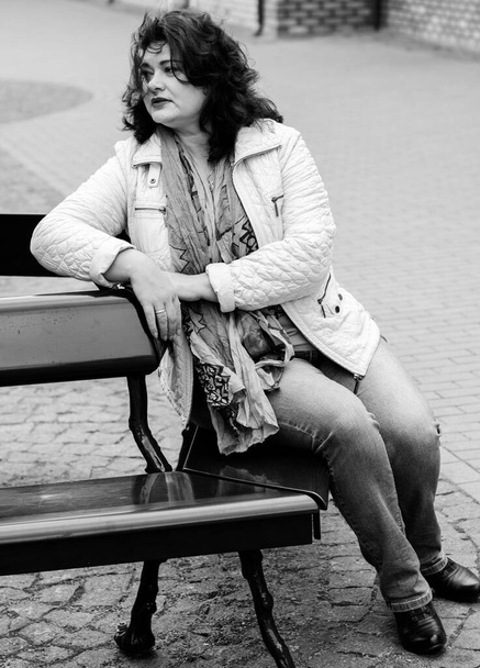 Mature simple woman of plus size, American or European appearance walks in the city enjoying life. Cute lady with excess weight, dressed in jacket and scarf going around old part of town - Photo, Image