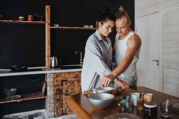 Young couple in love cook healthy food in the kitchen together. The girl has a face in flour - Фото, изображение