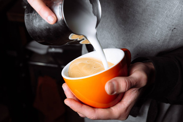 Barista ręce wylewanie ciepłego mleka w filiżance kawy do tworzenia sztuki latte. Zamknij się. - Zdjęcie, obraz