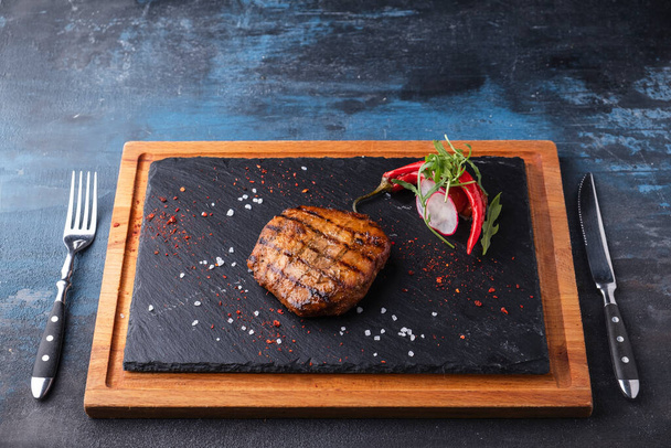 フォークとナイフで提供される黒い石の上にジューシーなグリルビーフステーキ。おいしい焼き肉 - 写真・画像