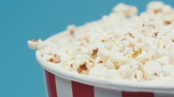 Selektivní zaměření popcornu ve velkém papírovém kbelíku, který se točí izolovaně na modré - Záběry, video