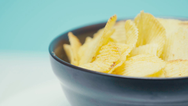 Selektiver Fokus von geriffelten Chips in schwarzer Schüssel, die sich auf blauem Hintergrund dreht  - Filmmaterial, Video