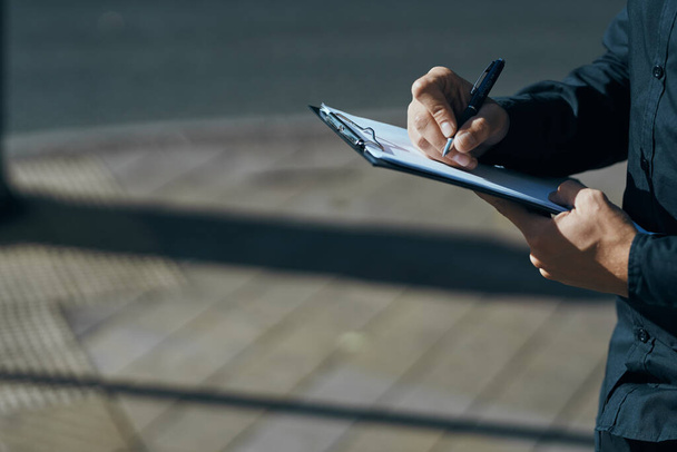 Человек с документами в руках в черных рубашках на улице с ручкой в руке - Фото, изображение